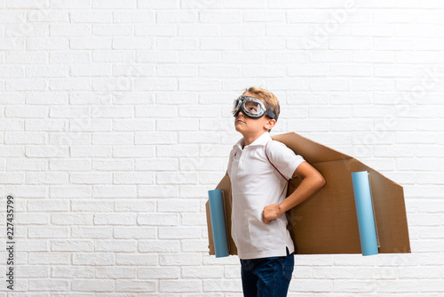 Boy playing with cardboard airplane wings posing with arms at hip