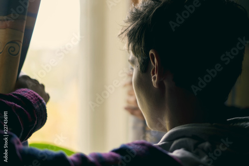 young sad teenager looking through the window f