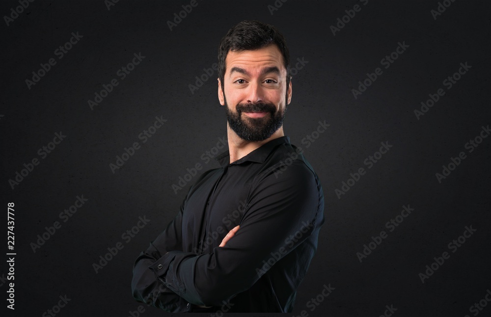 Obraz premium Handsome man with beard with his arms crossed on black background