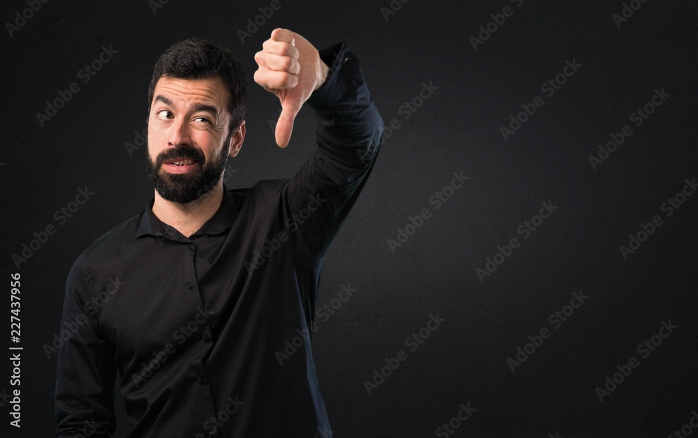 Handsome man with beard making bad signal on black background