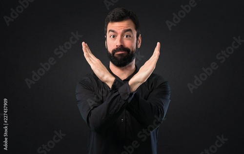 Handsome man with beard making NO gesture on black background