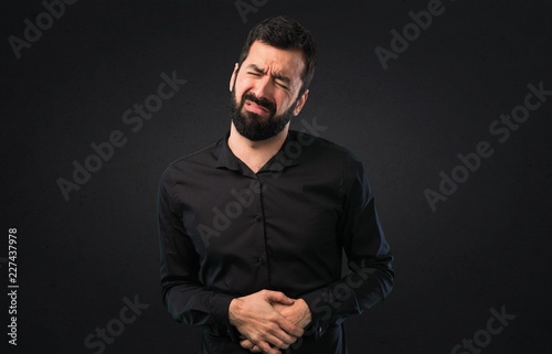 Handsome man with beard with stomachache on black background