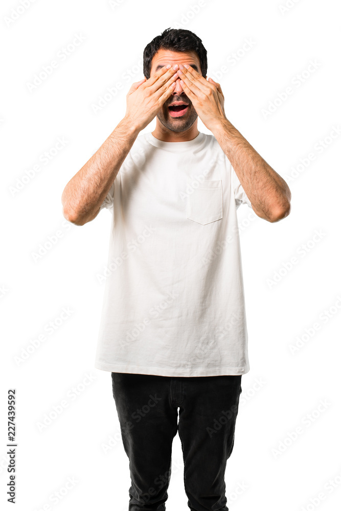 Young man with white shirt covering eyes by hands. Surprised to see what is ahead on isolated white background Young man with white shirt covering eyes by hands. Surprised to see what is ahead on isolated white background