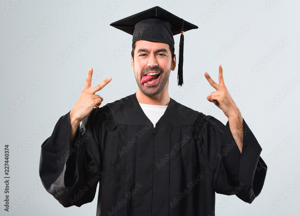 Man on his graduation day University showing tongue at the camera having funny look on grey background Man on his graduation day University showing tongue at the camera having funny look on grey background