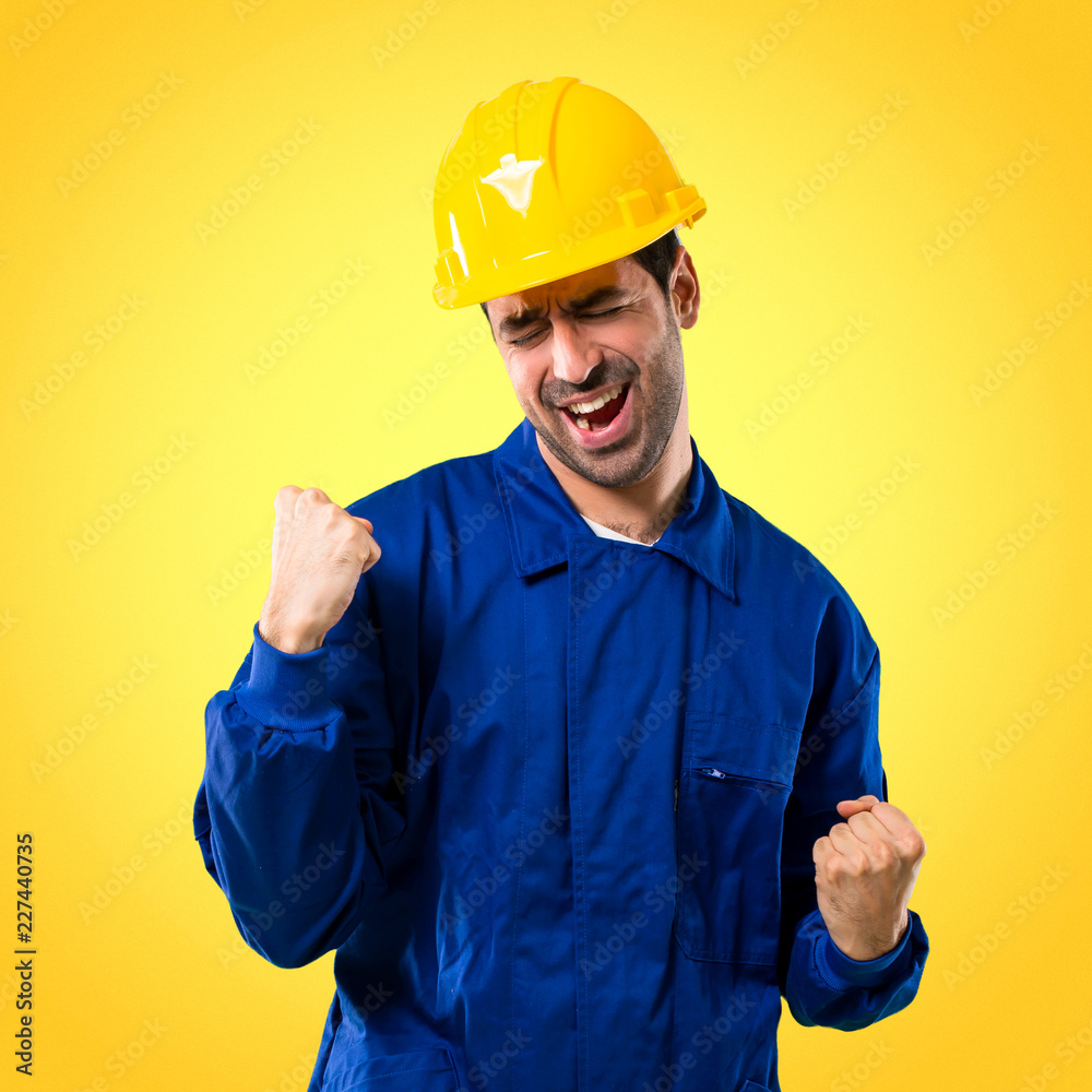 Young workman with helmet celebrating a victory and happy for having won a prize on yellow background