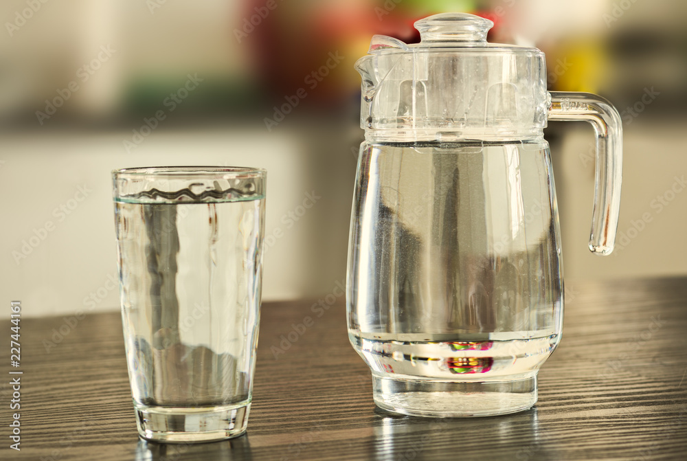 Pitcher and glass of water on kitchen background.