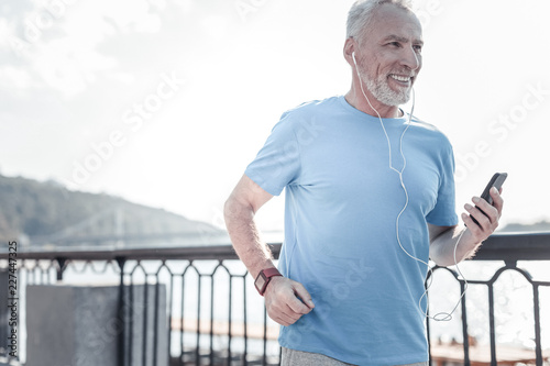 Music lover. Positive delighted man holding his telephone and wearing smart watches while doing sport
