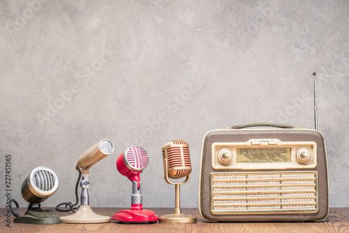 Retro portable broadcast radio receiver from circa 1950s and four microphones front textured concrete wall background. Interview or press conference concept. Vintage old style filtered photo