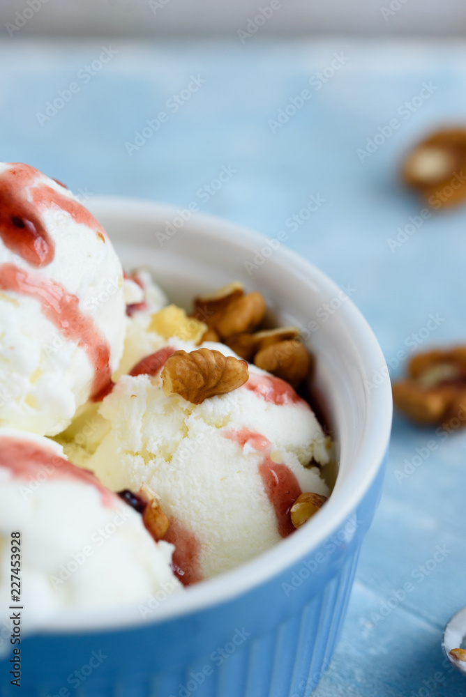 Vanilla ice cream with walnuts and fruit syrup in a blue bowl. Vanilla ice cream with walnuts and fruit syrup in a blue bowl.