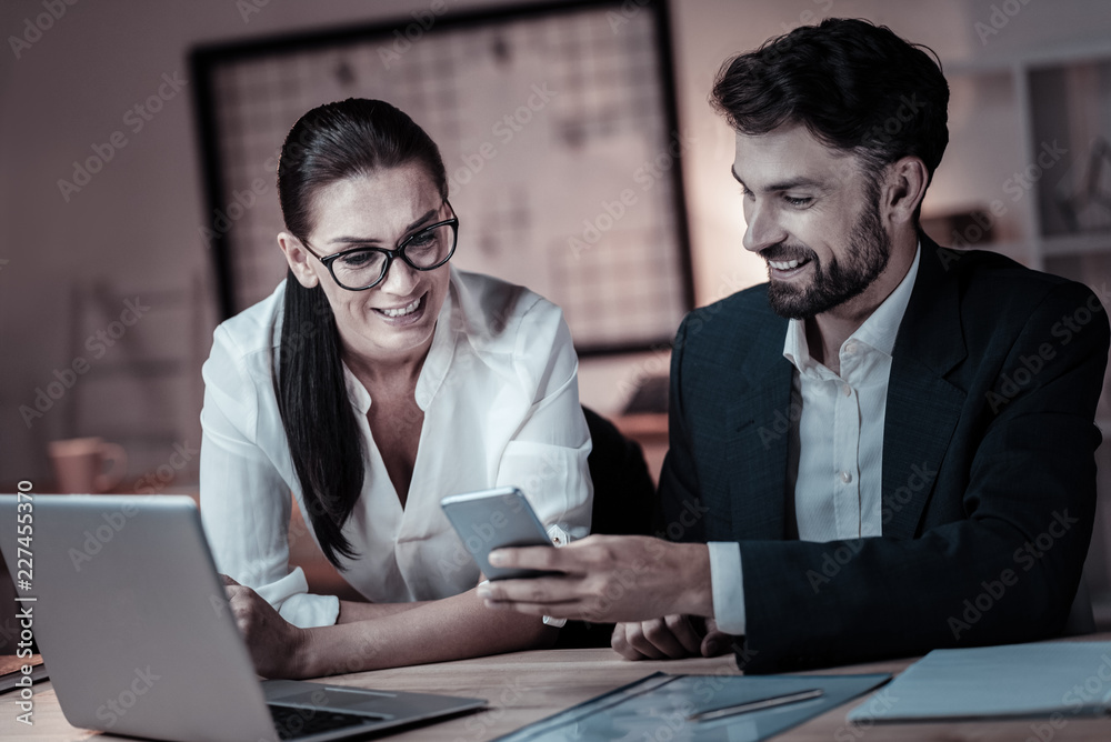 Fototapeta premium That is great. Attentive female expressing positivity and leaning on the table while looking at telephone