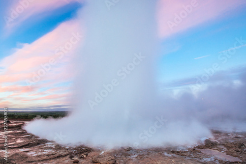 Strokkur geyser eruption in Iceland. Fantastic colors shine through the steam. Beautiful pink clouds in a blue sky