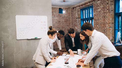 Morning meeting. Group of five young people discussing something while sitting at the table in office together. startup
