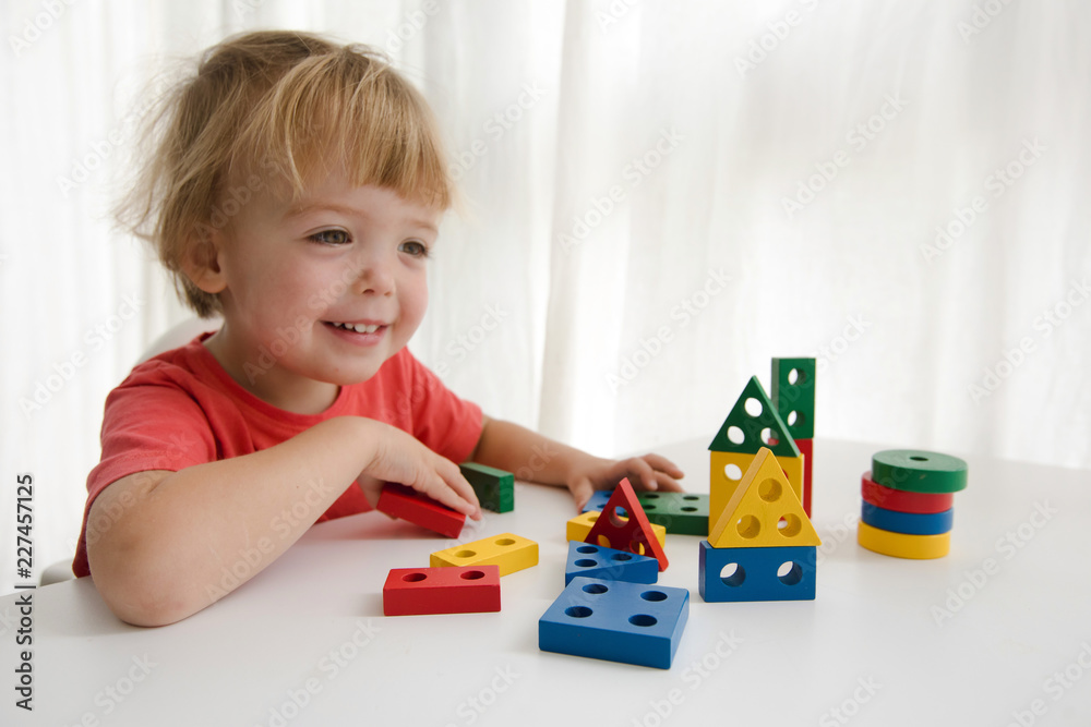 Charming infant boy sitting at table and playing with colorful constructor blocks isolated on white background Charming infant boy sitting at table and playing with colorful constructor blocks isolated on white background