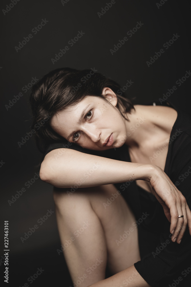 Portrait of sad woman sitting in front of black background Portrait of sad woman sitting in front of black background
