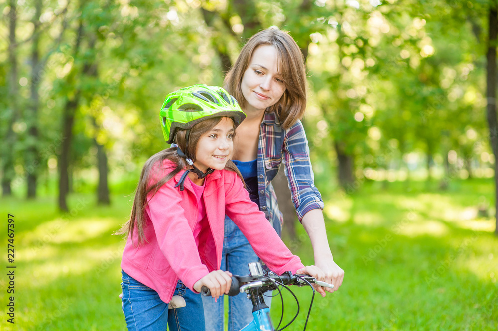 Happy family. Smiling mom teaches her daughter to ride a bicycle in the park Happy family. Smiling mom teaches her daughter to ride a bicycle in the park