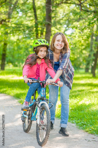 Happy family. Smiling mom teaches her daughter to ride a bicycle in the park