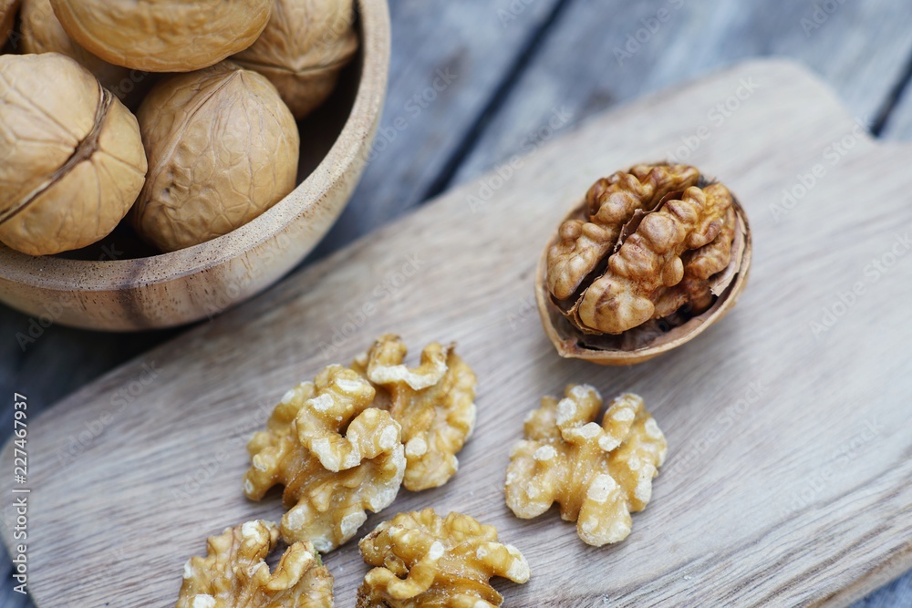 Walnut nut in wooden bowl on wood table with green leaf background, copy space Walnut nut in wooden bowl on wood table with green leaf background, copy space