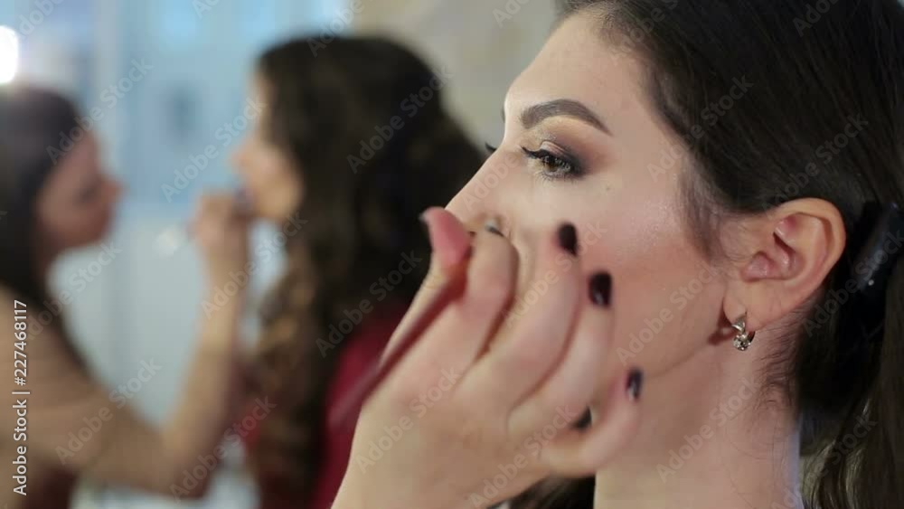 The make-up artist paints the lips of young girl. Make-up artist doing makeup for the young girl, close-up. In the background works with the client makeup artist, blurred background. The make-up artist paints the lips of young girl. Make-up artist doing makeup for the young girl, close-up. In the background works with the client makeup artist, blurred background.