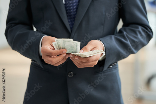Close-up of businessman in black suit counting dollar currencies
