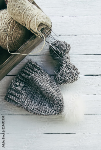 Knitted warp wainter cap with fluffy pompon and woolen grey yarn on white wooden background photo