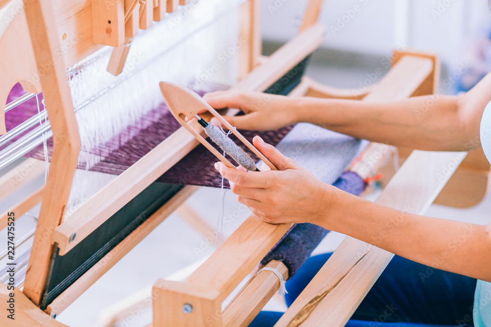 Obraz premium Women's hands weave a lilac canvas of thread on a weaving machine