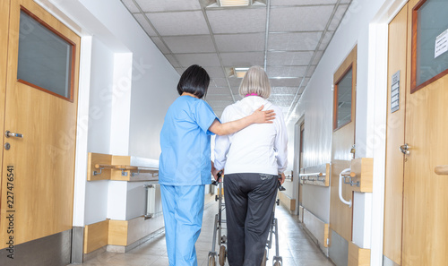 Asian doctor helping elder woman with walker in hospital hallway