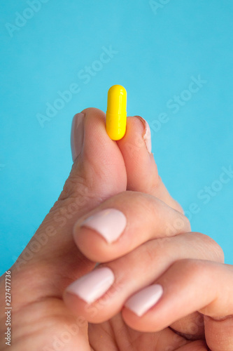 woman hand holding yellow pill capsule on blue background, medication concept with copy space