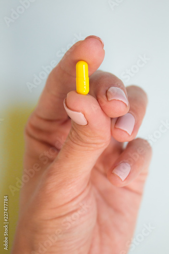 woman hand holding yellow pill capsule on light blue background  medication concept