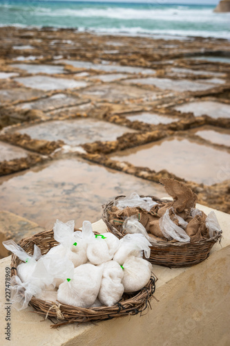 Salinas. Salt Pans or salters at the background with salt bags ready for sale in a basket or bowl outdoor. Hand harvest salt in Gozo Island Marsalforn. space for text. photo