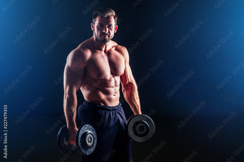 Muscular bodybuilder male fitness model antique statue perfect muscles six pack abs and bare nude chest doing exercises with dumbbell sexy man in the gym black background studio