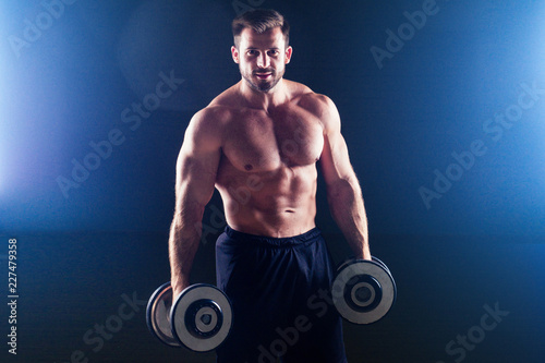 Muscular bodybuilder male fitness model perfect muscles six pack abs and bare nude chest doing exercises with dumbbell sexy man in the gym black background studio