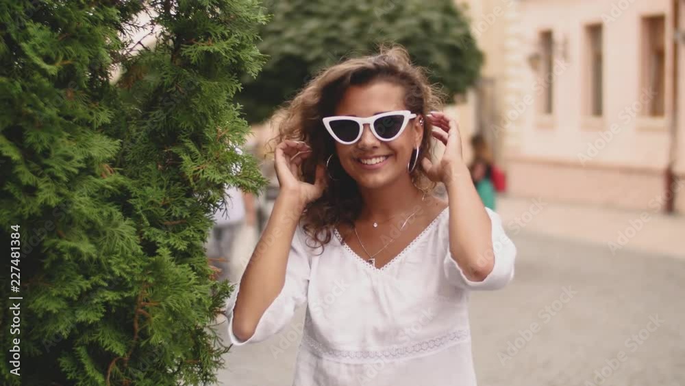 Pretty young curly woman looking straight to camera in cheerful mood with a happy smile, wearing stylish sunglasses Pretty young curly woman looking straight to camera in cheerful mood with a happy smile, wearing stylish sunglasses