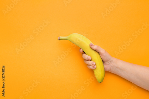 Female hand holding banana on orange background