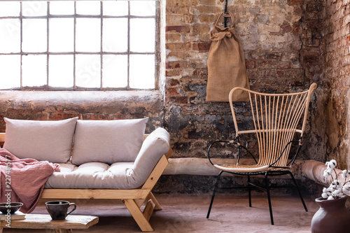 Armchair next to grey sofa with cushions in industrial interior with window and red brick wall. Real photo