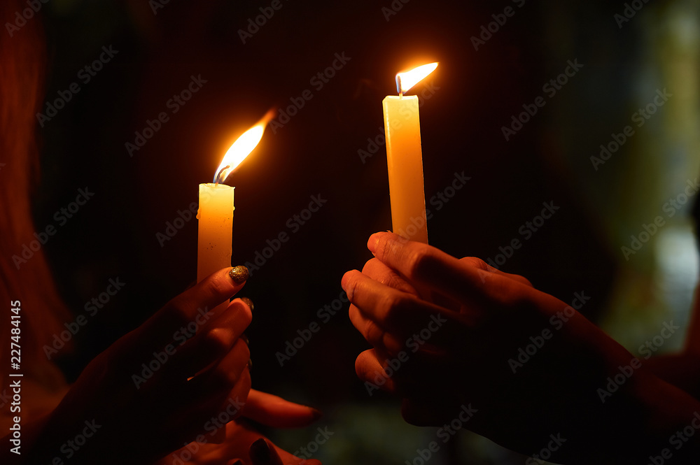 Naklejka premium hands holding a burning candle in dark