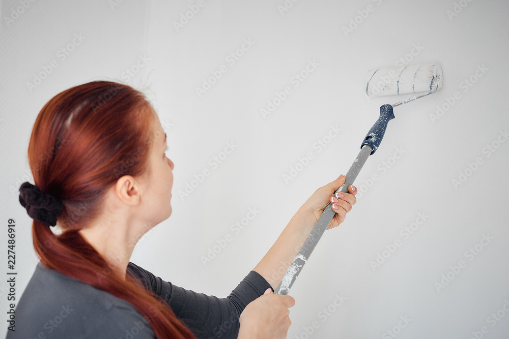 Caucasian woman painting with a roller the walls in the apartment