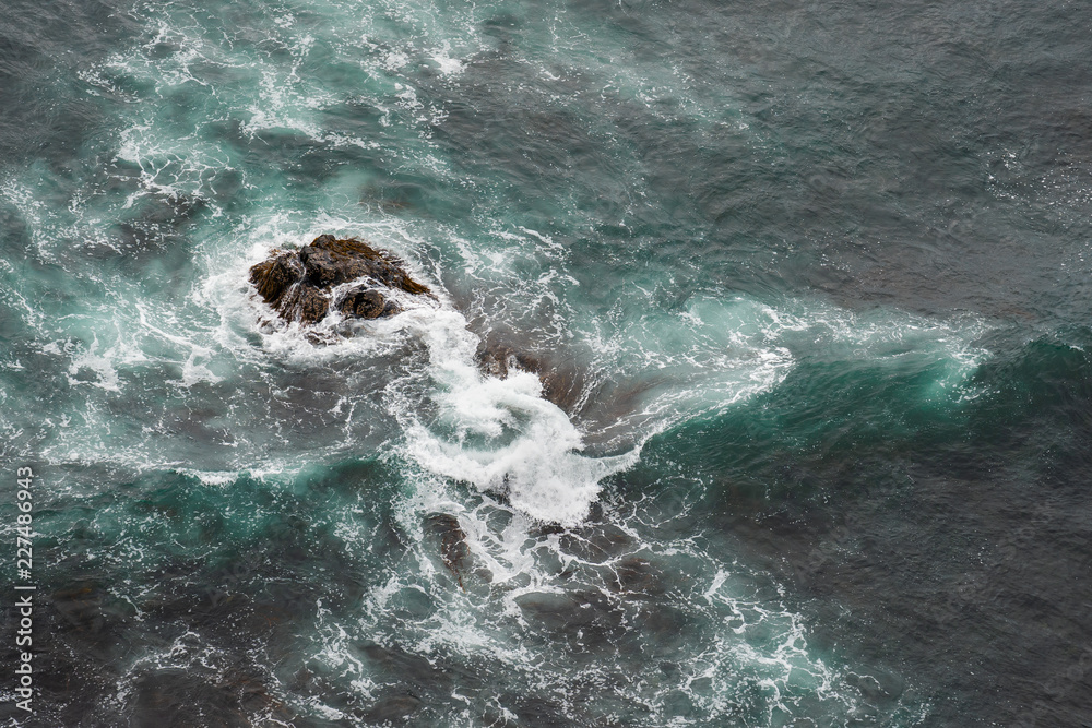 White ocean waves crashing over coastal sea rocks in summer.