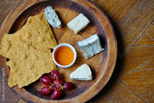 Gourmet cheese platter with honey, grapes and crackers on a wooden board