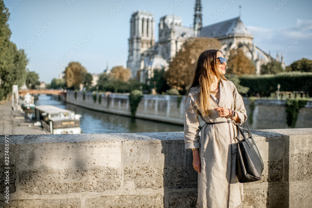 Lifestyle portrait of a young woman walking on the bridge with famous cathedral on the background in Paris, France