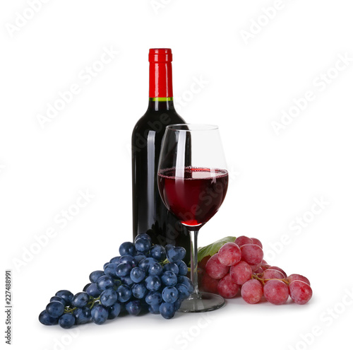 Glassware of red wine with ripe grapes on white background