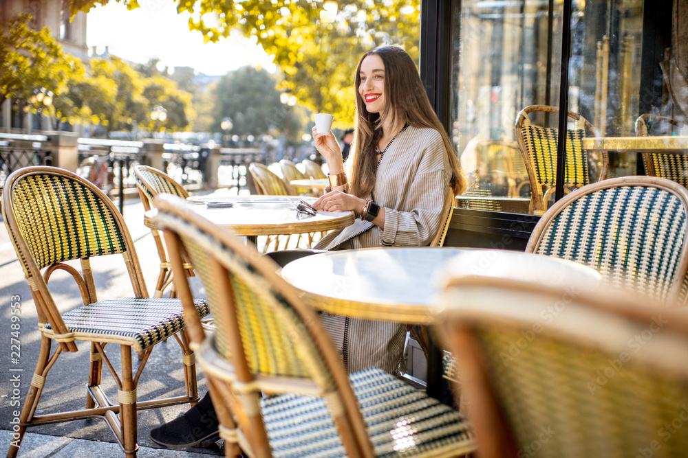 Portrait of a young woman enjoying coffee sitting outdoors at the traditional french cafe during the morning in Paris