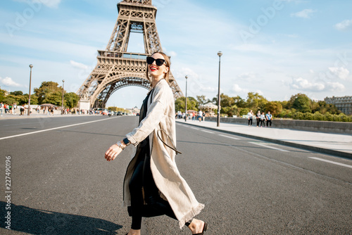Lifestyle portrait of a young stylish woman crossing the street in front of the famous Eiffel tower during the sunny day in Paris