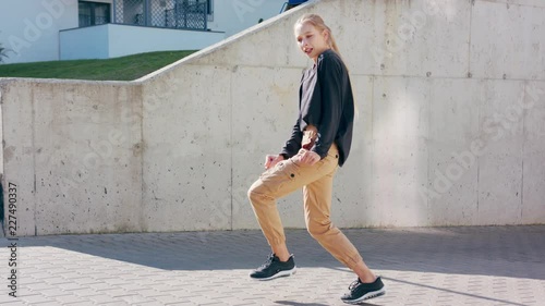 A young girl performs modern hip hop dance on the streets of the city during the summer, twisting and rotating.