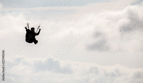 Paragliding pilot silhouette in the fluffy clouds sky.