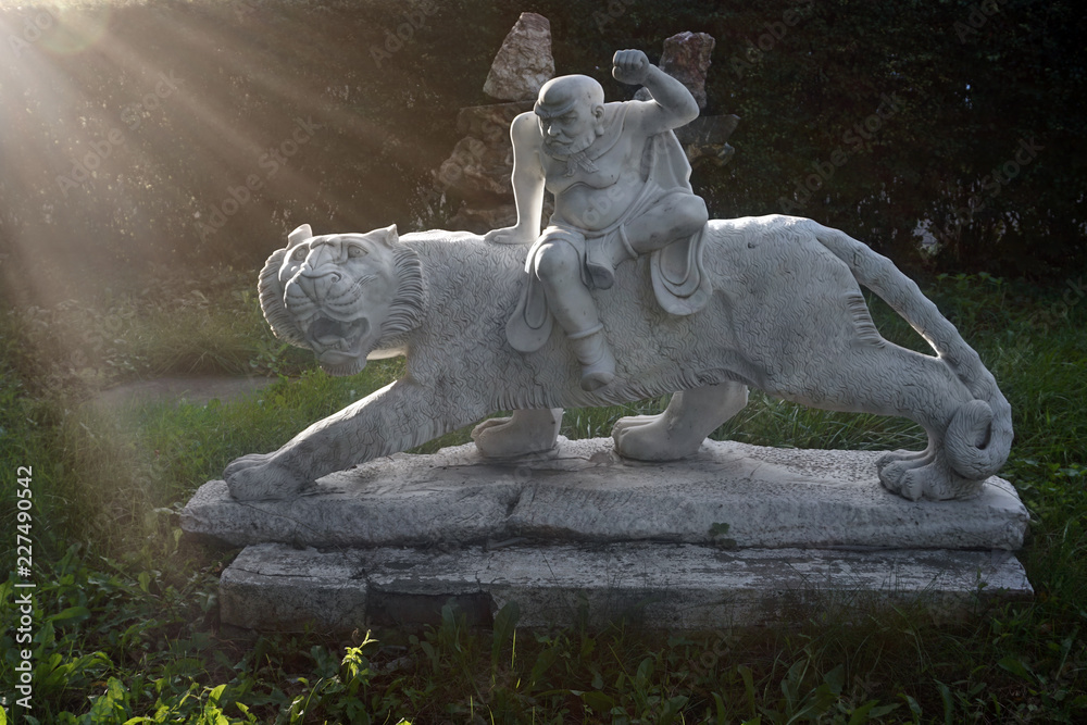 Marble sculpture of chinese tiger and warrior in a garden with green grass and sunset sun as background Marble sculpture of chinese tiger and warrior in a garden with green grass and sunset sun as background