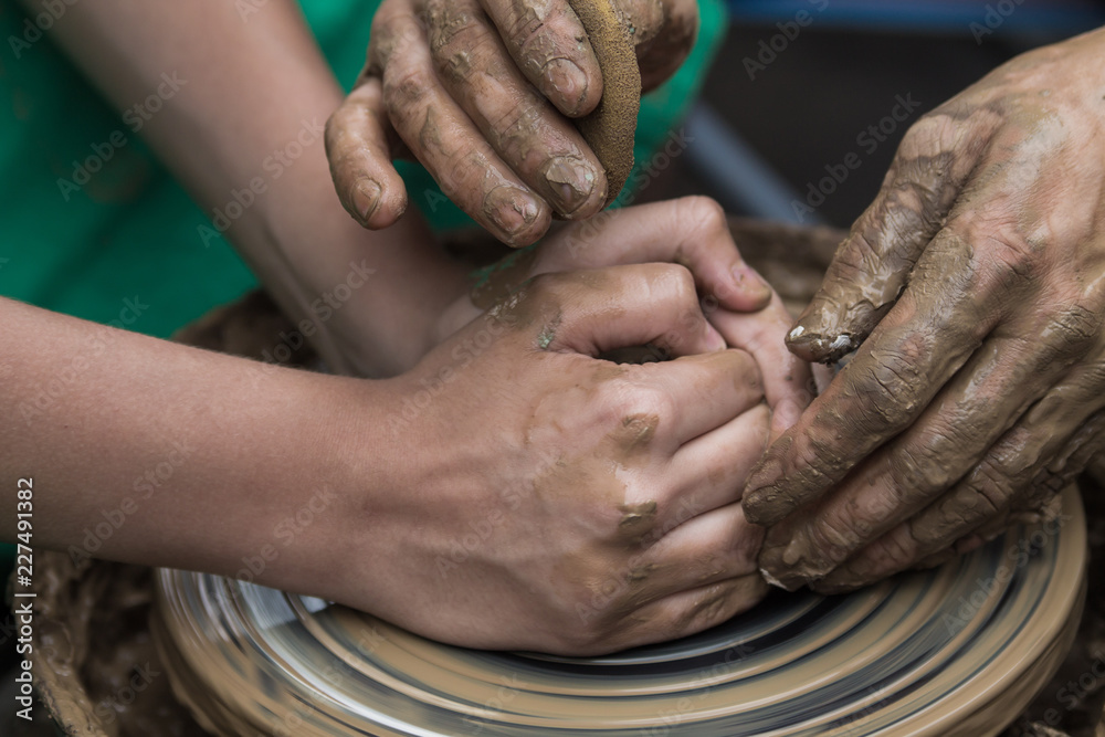 Fototapeta premium hands of a potter, helping to a boy create an earthen jar on the circle