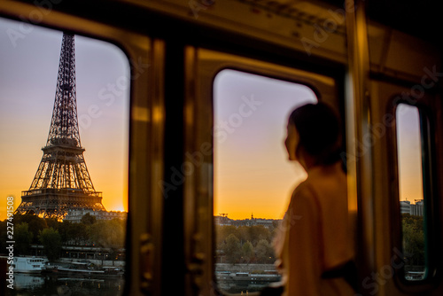 Young woman enjoying view on the Eiffel tower from the subway train during the sunrise in Paris. Image focused on the background