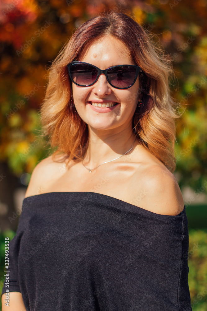 Charming woman in a black dress and sunglasses in the autumn park
