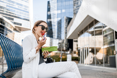 Принти на полотні Business woman having a snack with lunch box during a break sitting outdoors at