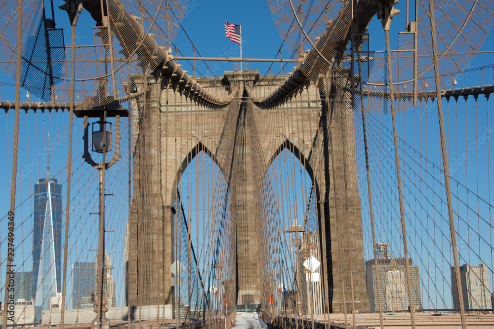 Fototapeta premium Detail of Brooklyn Bridge, New York City showing stone tower and American flag against a blue sky